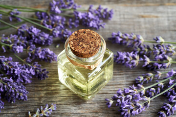 A bottle of essential oil with blooming lavender twigs on wood
