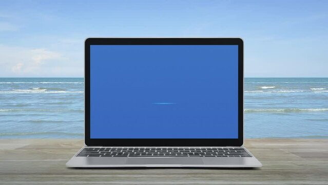 Power button icon on modern laptop computer screen on wooden table over tropical sea and blue sky with white clouds, Business start up online concept
