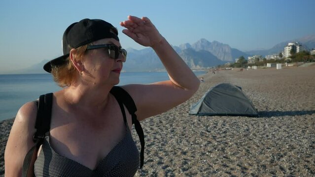 Senior adventure is ageless woman with backpack on sea beach near tent in Antalya Turkey. Summer active tourism for pensioner.