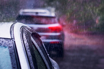 Heavy rain falls on the roof of a car during a thunderstorm. Red brake light in the dark. The concept of auto insurance and natural disasters. Driving on cloudy rainy days. Selective focus. - obrazy, fototapety, plakaty