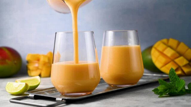 Pouring mango smoothie in a glass with fresh mango, mint and lime.