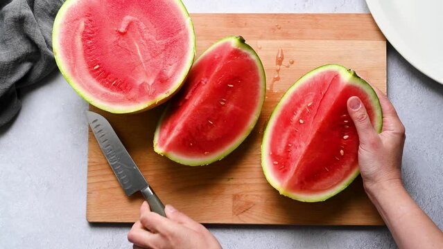 Female hands cutting fresh juicy watermelon on cutting board.
