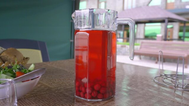 Ripe red dogwood fruits in glass carafe, next to jug of compote on old wooden table. Concept of healthy eating. Homemade bottle of Dogwood Compote, sweet drink with boiled fruit