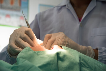 Professional dentist in medical mask and latex gloves examining teeth of male patient with open mouth on dental unit at modern dental clinic in the hospital.