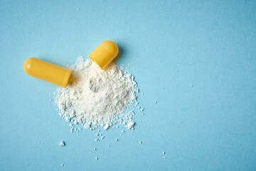 scatter powder from yellow gelatin capsule pills, open oral medical drug filled with powder on blue background, taken straight from above with copy space