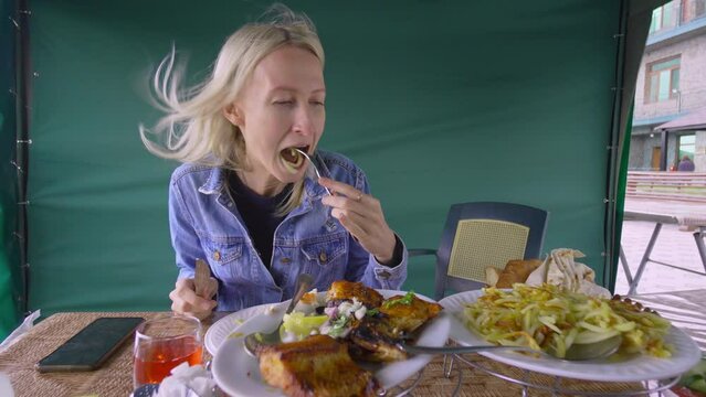 Happy woman eating fried fish in Restaurant and chatting, speaking on camera. On table is red dogwood compote, potatoes, salad. Dinner at diner and cheap table. Restaurant Cheap.
