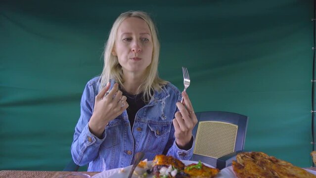 Happy woman eating fried fish in Restaurant and chatting, speaking on camera. On table is red dogwood compote, potatoes, salad. Dinner at diner and cheap table. Restaurant Cheap.