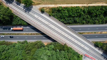 This stunning aerial shot captures the organized beauty of a Belgian highway on a bright summer day. The road, with its impressive bridge, threads through vast expanses of lush forests and fields