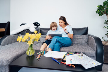 Mother and son on the sofa using digital tablet. Happy mom and little boy using touch screen tablet...