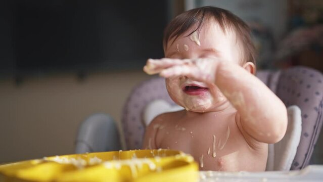 baby eats dirty. happy family a kid toddler concept. baby girl dirty sitting messing with food at the table for feeding in the kitchen. grimy toddler lifestyle in the kitchen