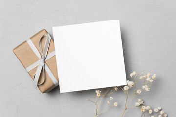 Blank square card mockup with gift box and dry flowers decor, top view with copy space