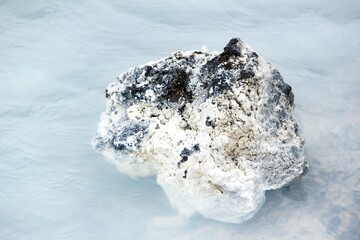 Black rock in milky white waters of Icelandic thermal nature baths near blue lagoon