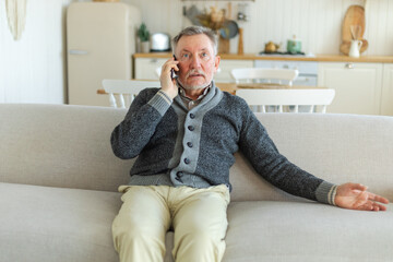 Fototapeta premium Happy middle aged senior man talking on smartphone with family friends. Older mature grandfather with cell phone talking with grown up children, resting at home. Older generation modern tech usage