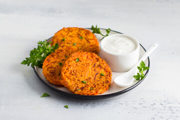 Carrot fritters with sour cream and greens on a white plate on a light blue background