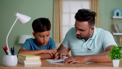 Indian father teaching or helping the son for reading from book at home - concept of Parental Guidance, home education and Tutoring Sessions.