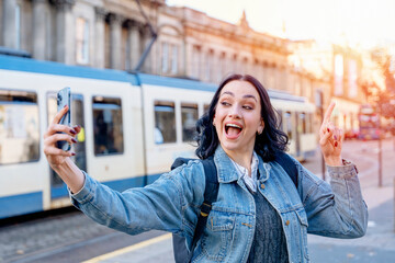 Outdoor portrait of happy woman in denim jacket using mobile phone on tram stop