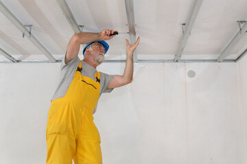 Senior adult worker placing aluminum profile for gypsum ceiling and insulation using screwdriver