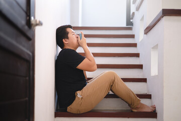 Sick Asian young man using inhaler to treat asthma and respiratory diseases at home. Asthma attack. Concept of allergy care.