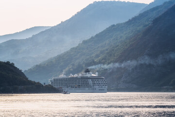 Amazing view of a large cruise ship passing near the beautiful city of Perast and leaving the picturesque bay of Kotor (Boka Kotor) in Montenegro