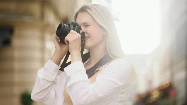 Portrait of pretty young blond woman photographer hold digital camera and looking around at urban city Charming tourist female taking pictures and enjoying beautiful day outdoors