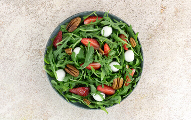 Salad with strawberries, mozzarella balls, arugula and pecans on pink background. Top view. 