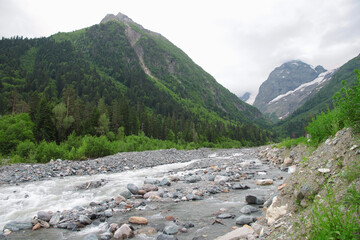 Mountain river flows between stones in the boundless mountains of the North Caucasus. Karachay-Cherkess Republic. Cloudy sky, selective focus.