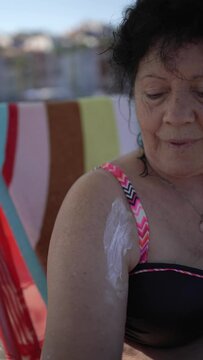 Older woman protecting her shoulder surgery scar. Vertical video of an nonymous woman on the beach covering with sunscreen the scar of a surgical intervention with shoulder prosthesis.