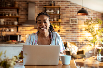 Young woman using a laptop in the morning while having breakfast in the kitchen