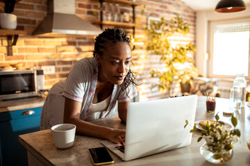 Young woman using a laptop at home in the kitchen - obrazy, fototapety, plakaty