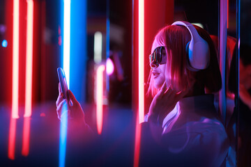Beautiful woman with purple hair in futuristic costume over dark background. Violet neon light. Portrait of young girl in modern headphones listening music.