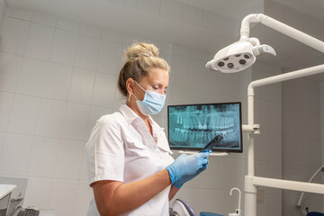 Female dentist hands sterile glove using smartphone at dentistry office over teeth xray on monitor. Orthodontist chatting with patients, searching information