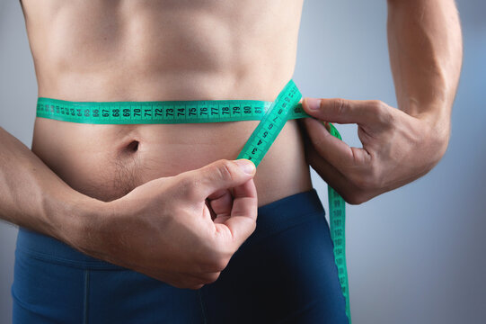 Close-up with waist and centimeter. The concept of a slim figure. Slim and athletic man in shorts checks his body. Body care. Weight loss and strong diet concept