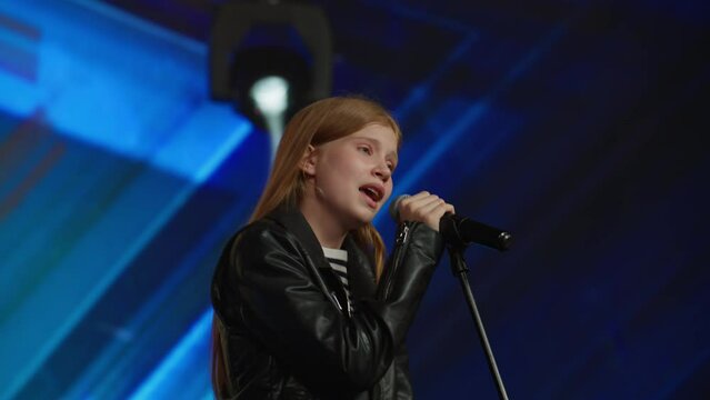 Young teenager girl singer performing on stage, contestant singing during recording of television style broadcast talent show