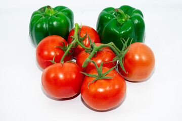 A group of red tomatoes next to fresh green pepper