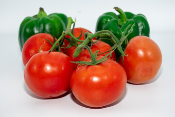 A group of red tomatoes next to fresh green pepper