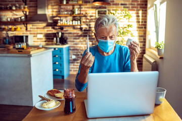 Senior man wearing a mask talking to his doctor over a video call while having breakfast in the morning