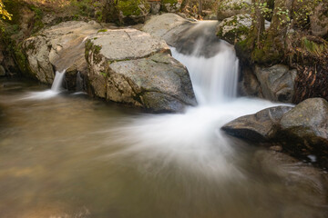 Small waterfall in a river whose flow runs between large granite stones deep in a dark forest. Concept of peace and relaxation, water stream and silk water.