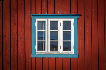 Obraz na płótnie Canvas White framed window on an old red plank wooden cottage, fishing hut rorbu. Typical north house trend. concept of scandinavian background