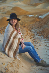 Beautiful woman in a hat with a plaid near a quarry at sunset