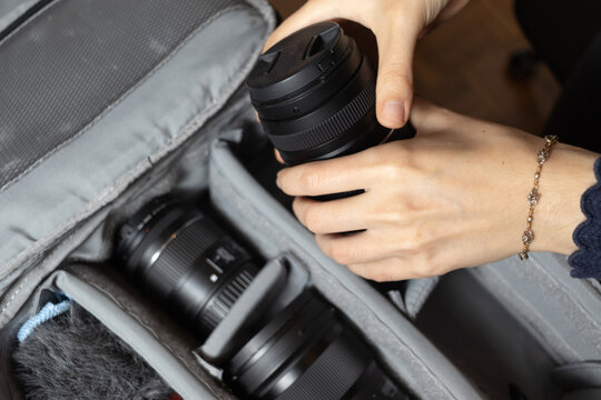 Woman's hands holding a photographer lens over travel photography backpack.