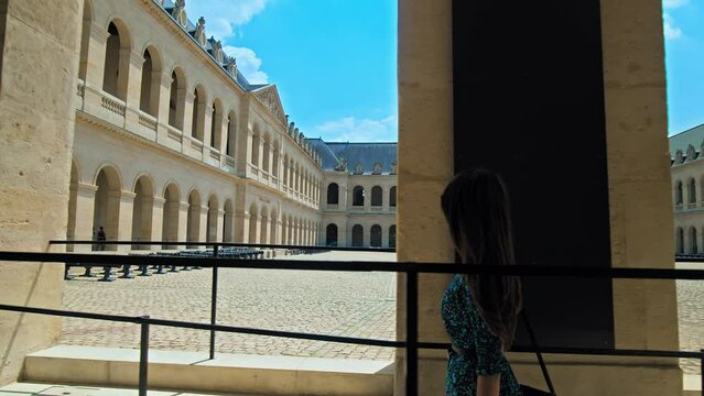A young woman visiting and taking pictures of The Court of Honor of Hotel National des Invalides in Paris. A tourist looking at the Golden Dome of the Hotel des Invalides and rooftops of Paris.