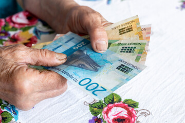 An old woman holds Norwegian kronor money in her hands, banknotes of different denominations, the concept of finances of pensioners