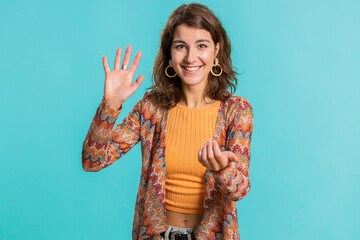 Come here, join us. Welcome. Brunette attractive woman showing inviting gesture with hands, ask to join, beckoning to coming, gesturing hello, goodbye. Pretty girl isolated on blue studio background