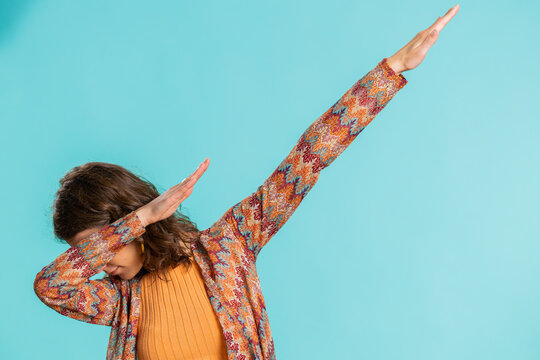 Trendy cheerful positive young woman having fun dancing and moving to rhythm, dabbing raising hands, making dub dance winner gesture. Happy girl isolated alone on blue studio background. Lifestyles