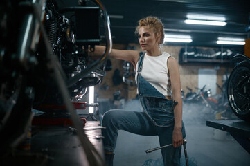 Fototapeta na wymiar Talented girl wearing blue jumpsuit using work tool to repair motorcycle