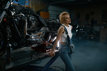 Fototapeta na wymiar Young blond woman mechanic at motorcycle workshop side view shot