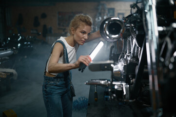 Obraz na płótnie Canvas Female bike technician using led lamp to detect malfunction in motorcycle