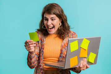 Exhausted freelancer woman with pasted sticker notes use laptop computer having concentration problem creative crisis, time out. Nervous girl confused by big routine work loading on blue background
