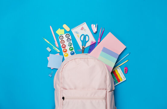 Pink school backpack with stationery on color background, top view