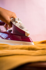 Close up of hand ironing yellow clothes with purple iron